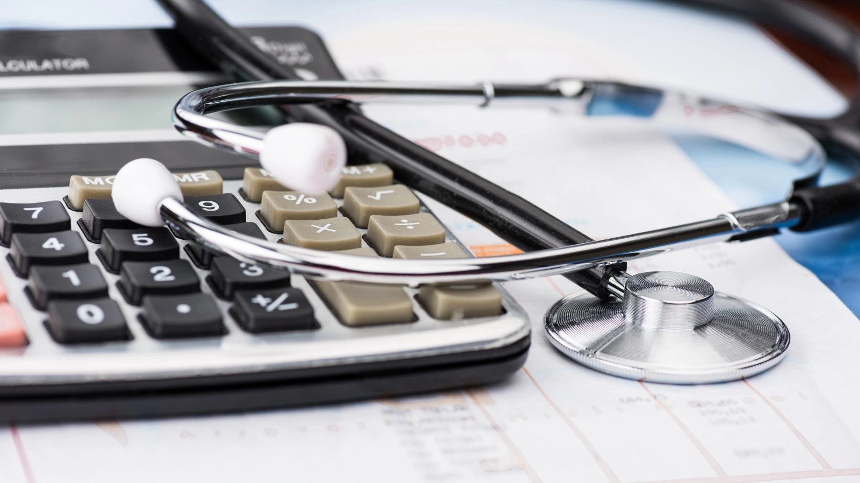 Ein Stethoskop liegt auf einem Taschenrechner und Unterlagen