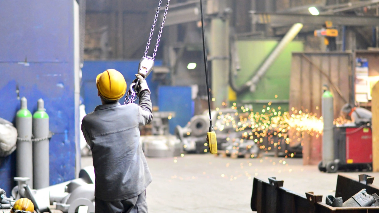 Ein Mann mit Schutzhelm hält eine Metallkette, die an einem Kran hängt.