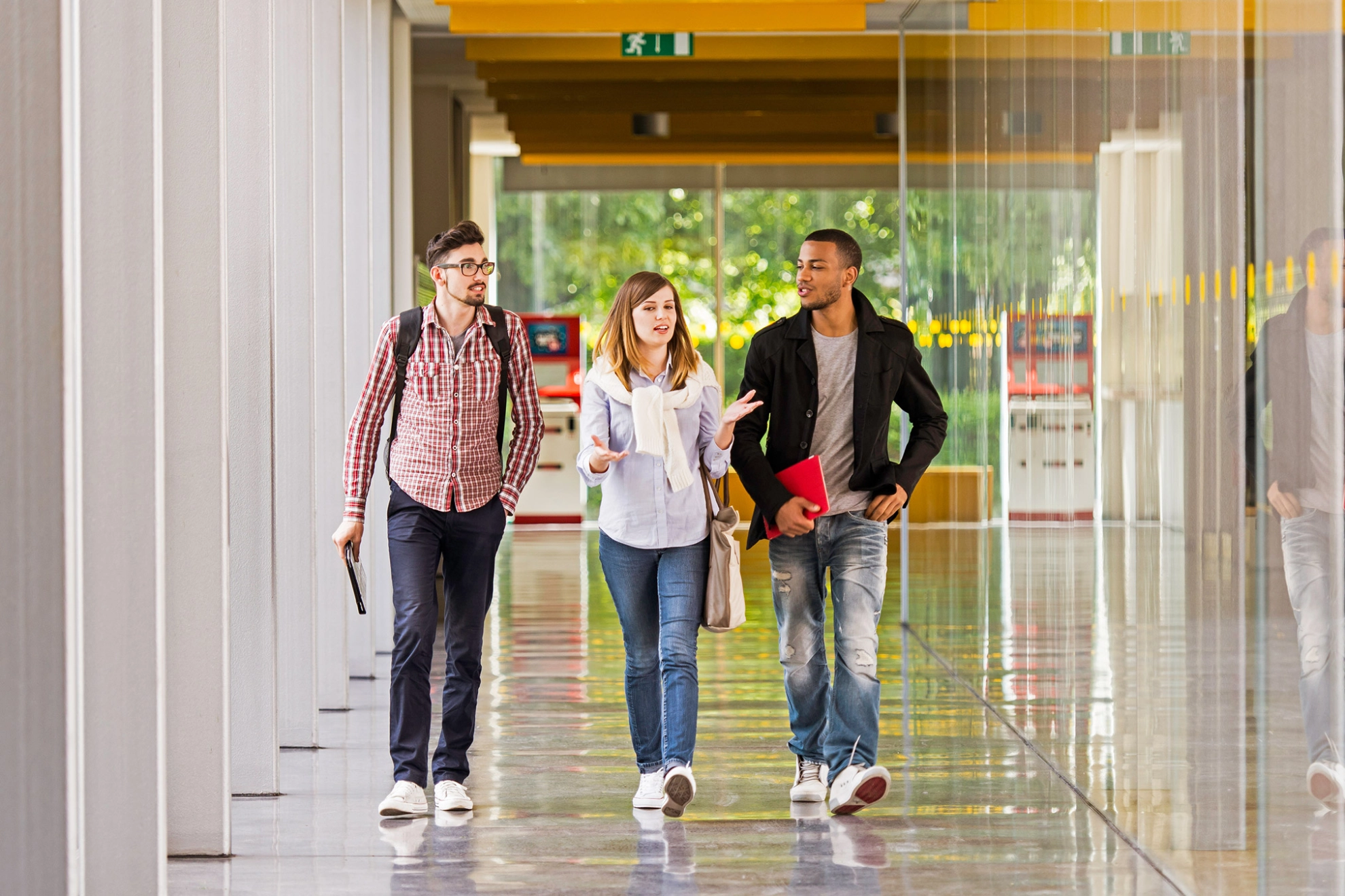 Eine Studentin und zwei Studenten laufen über einen Korridor und unterhalten sich dabei.